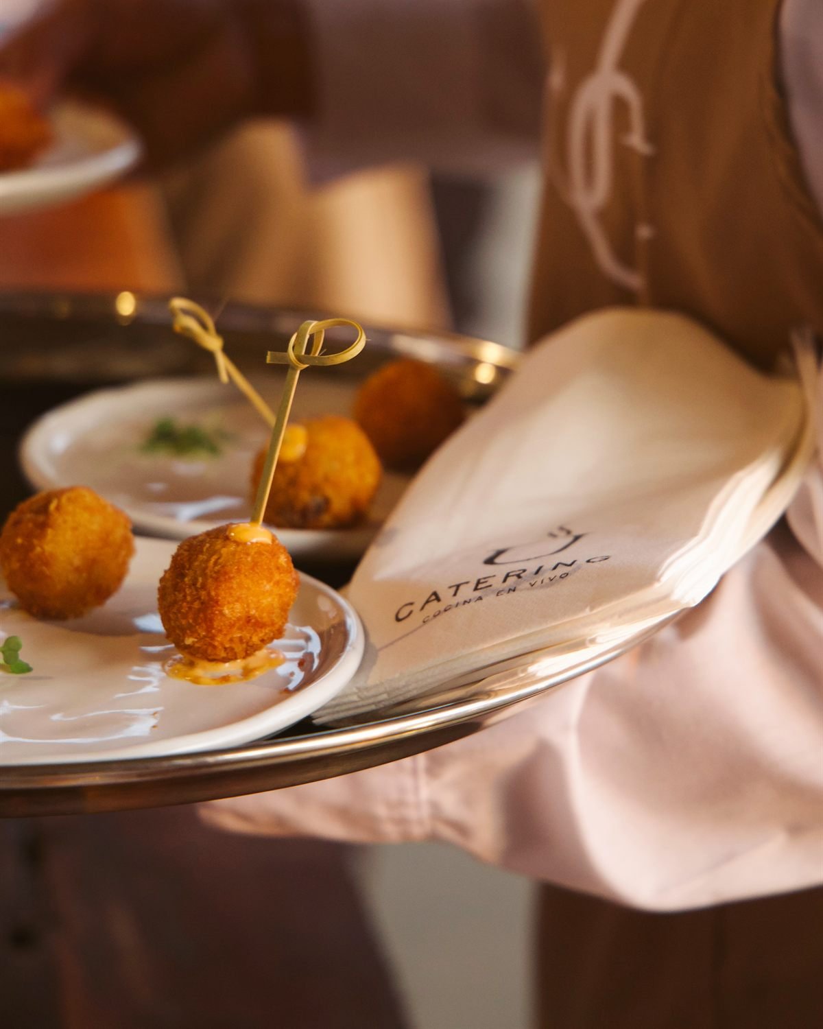 Camarero de U Catering llevando una bandeja de plata con croquetas y una servilleta con el logo de la marca